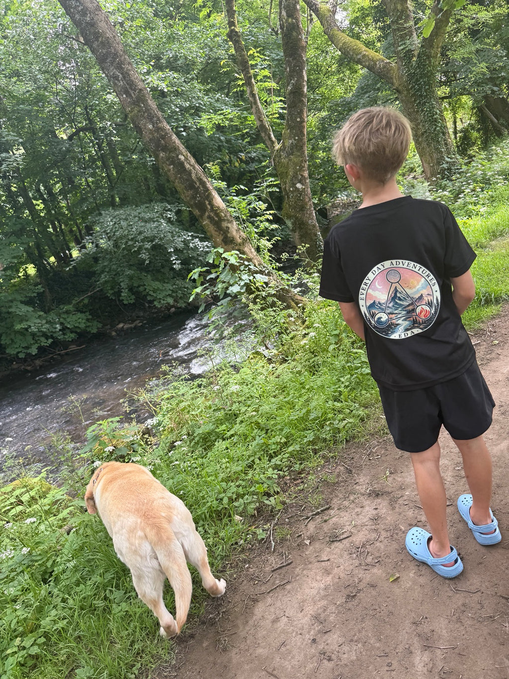 Young Explorer black EDA T-shirt worn beside a woodland stream